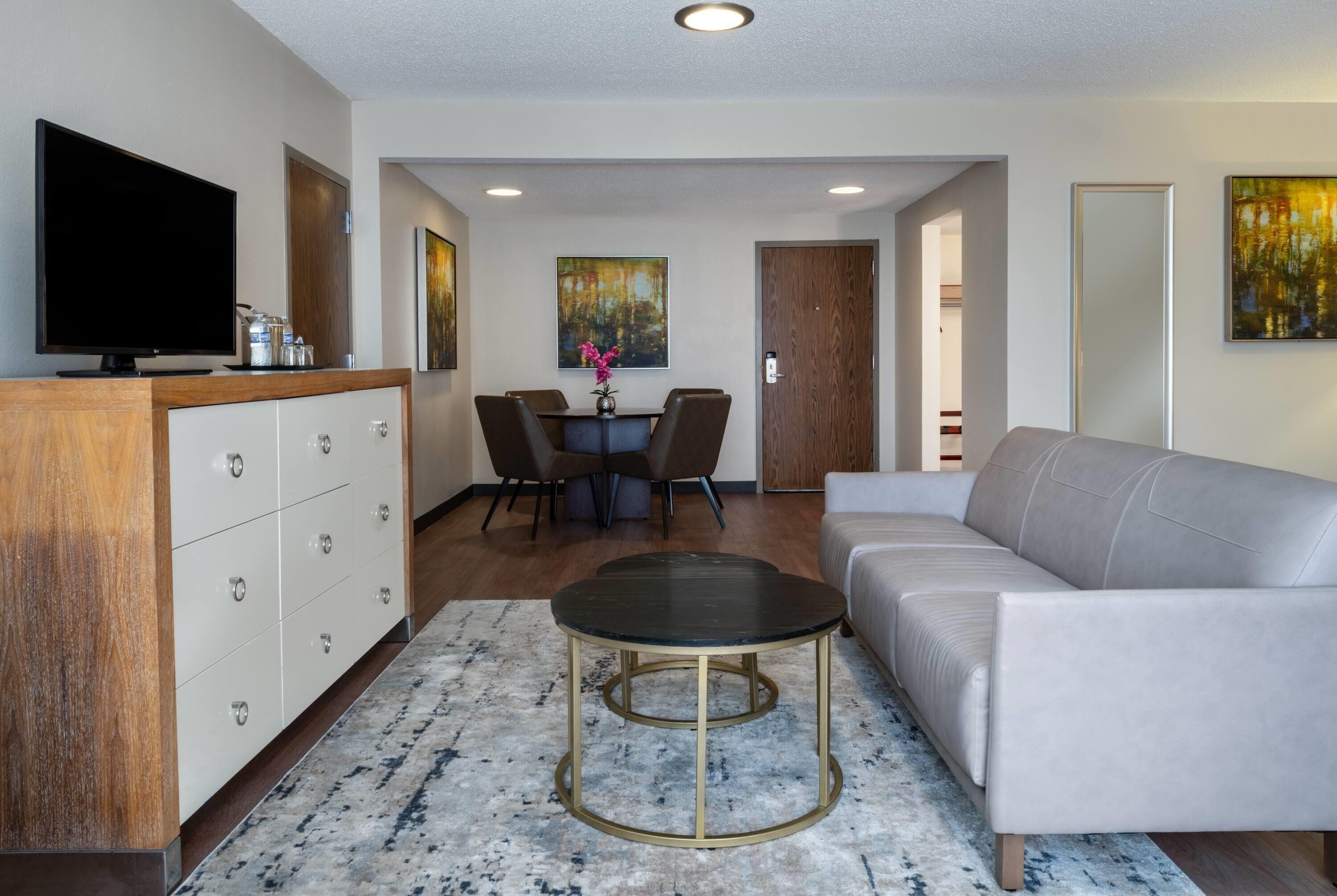 A modern living room with a sofa, a coffee table, a TV, and a dining area with chairs and a table.