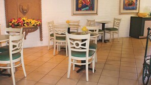 Un comedor con sillas y mesas blancas, un arreglo floral y dos obras de arte enmarcadas en la pared.