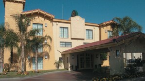 Un edificio grande de color beige, con techo de tejas rojas, múltiples ventanas y un vestíbulo cubierto.
