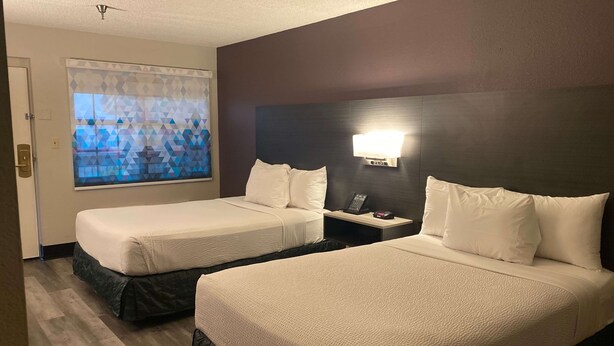 Habitación de hotel con dos camas, una mesita de noche, un teléfono y un ventanal con diseño geométrico.