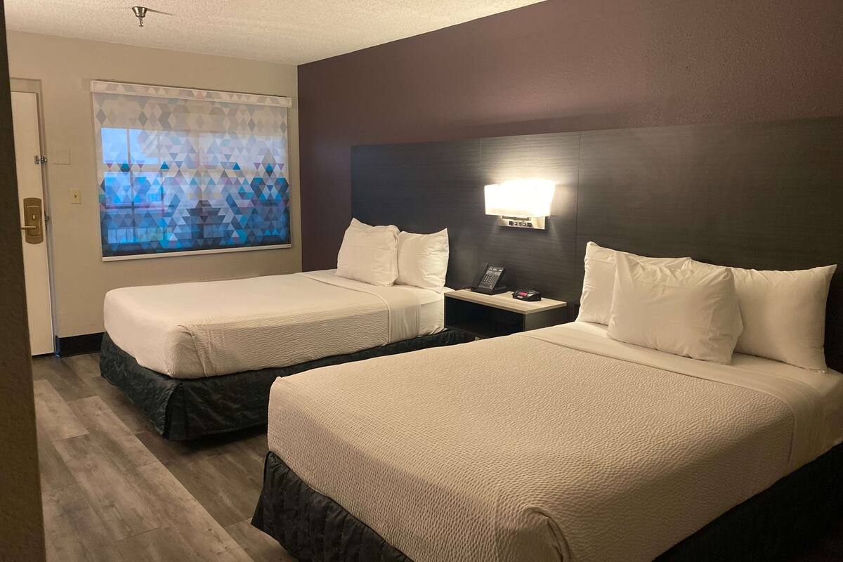 A hotel room with two beds, a nightstand, a phone, and a window with a geometric pattern.
