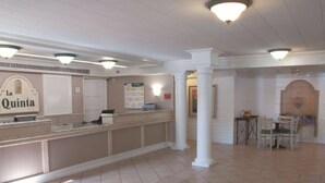 Zona de recepción con mostrador, columnas, suelo de baldosas y comedor con sillas y una mesa.