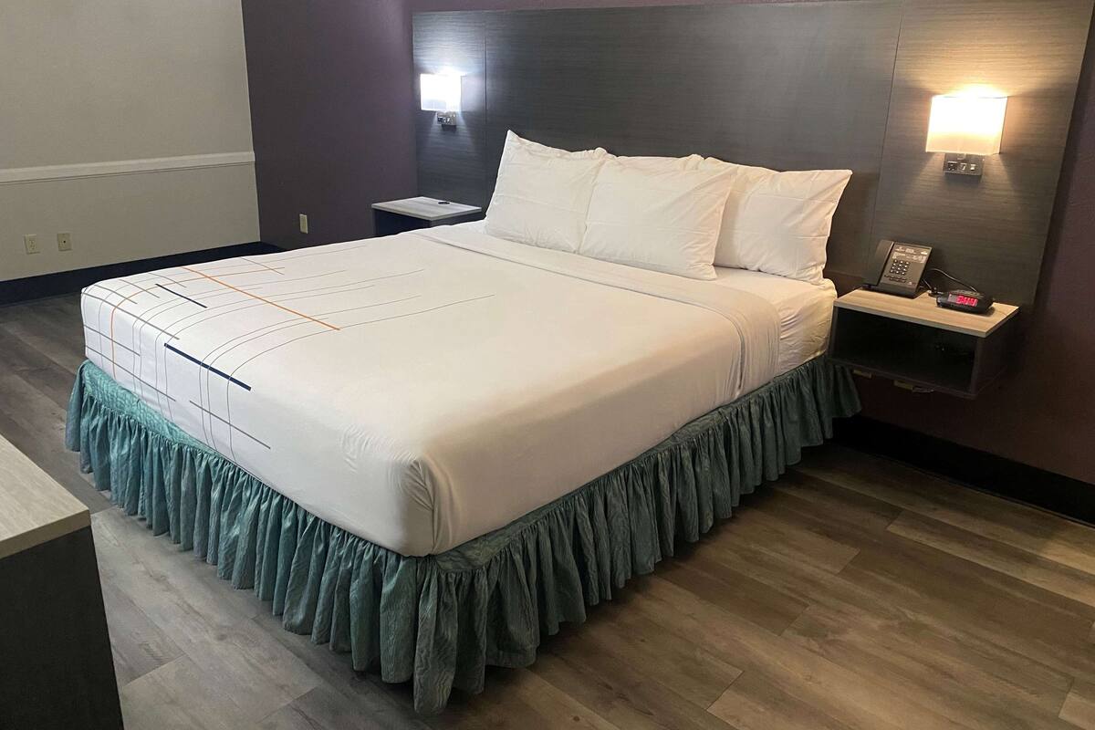A neatly made bed with a green skirt, two bedside tables with lamps, and a wall-mounted phone.