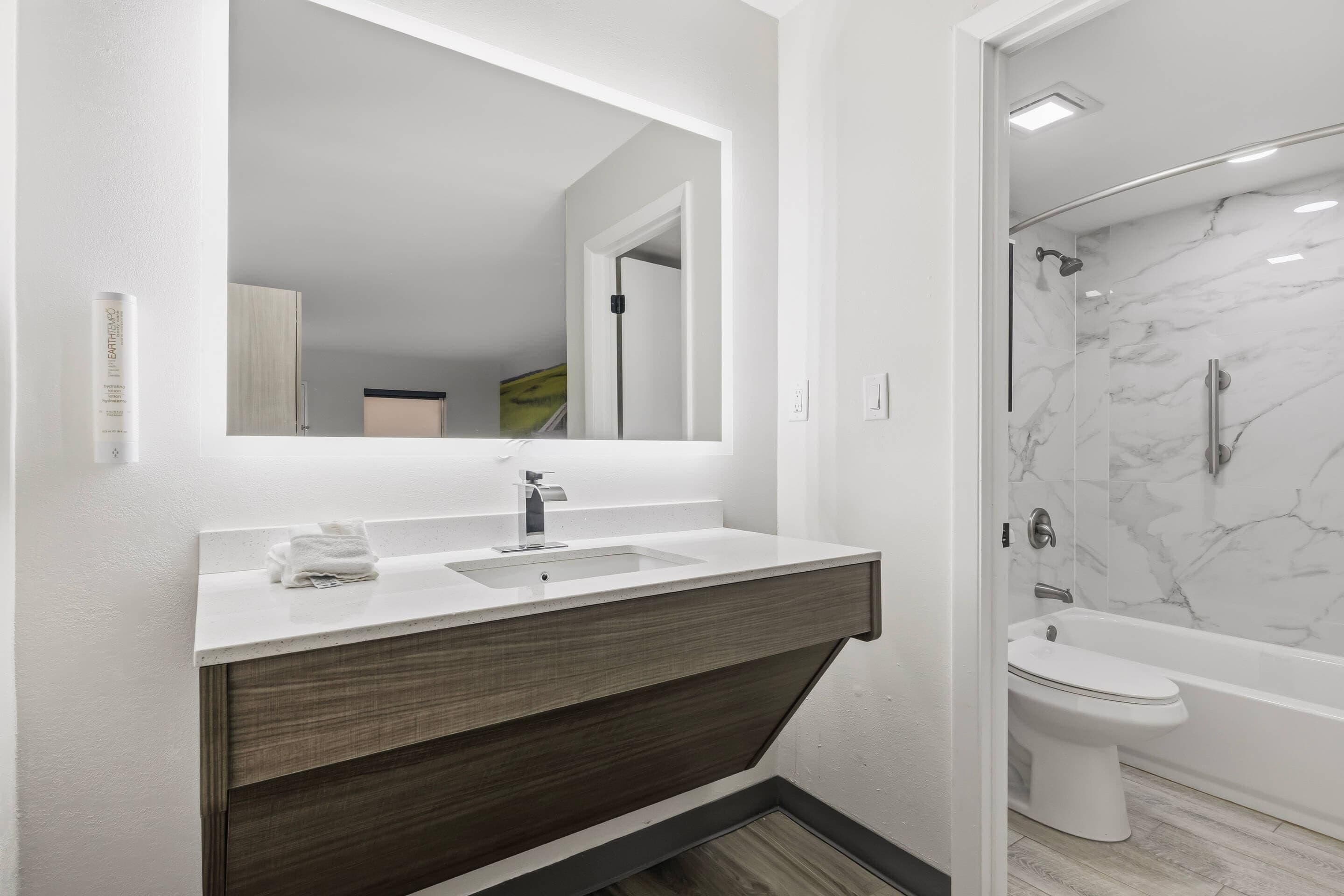 Un baño moderno con un espejo grande, un lavamanos, una ducha y un inodoro.
