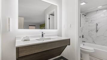 Un baño moderno con un espejo grande, un lavamanos, una ducha y un inodoro.