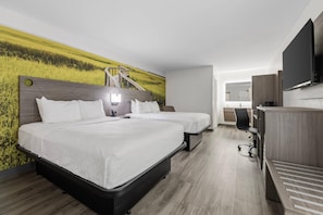 A hotel room with two beds, a wooden headboard, a flat-screen TV, a desk with a chair, and a bathroom visible through an open door. - Clarion Pointe Alachua - Gainesville Area (Alachua)
