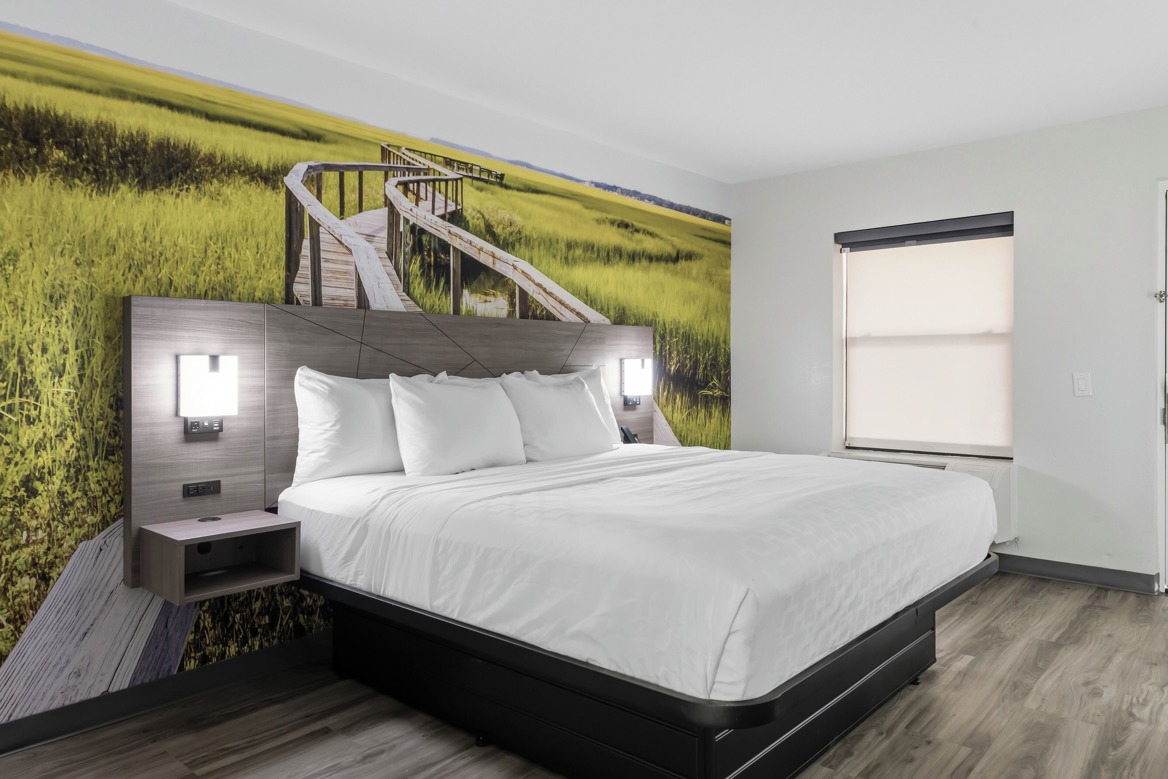 Een moderne slaapkamer met een groot bed, een hoofdeinde met ingebouwde verlichting, een nachtkastje en een muurschildering van een veld met een trap.