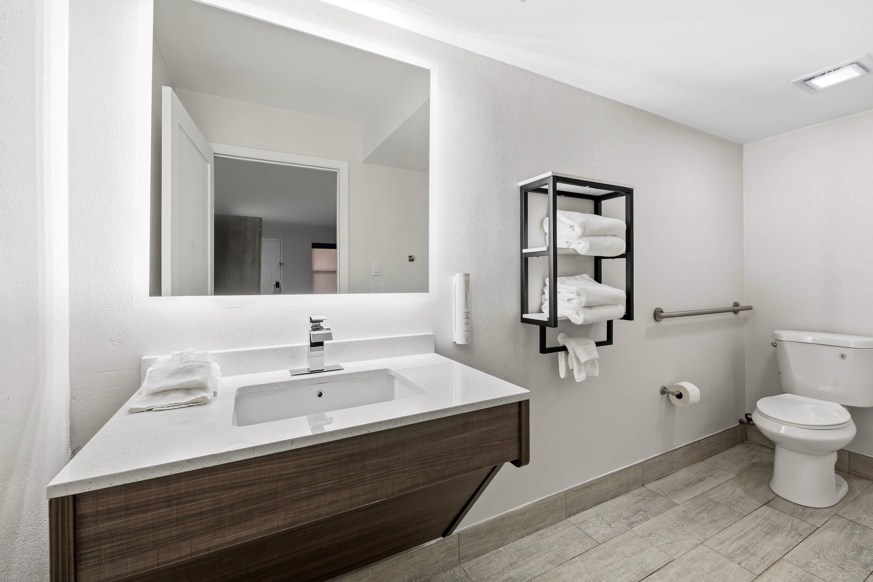 A modern bathroom with a white sink, dark wood vanity, a large mirror, a towel rack, and a toilet.