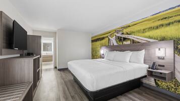 Habitación de hotel moderna con una cama grande, un televisor de pantalla plana, un escritorio y un mural con un paisaje.