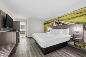 A modern hotel room with a large bed, a flat-screen TV, a desk, and a mural of a landscape.