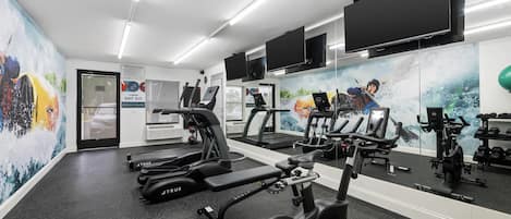 Un gimnasio con cintas de correr, bicicletas estáticas y pesas.