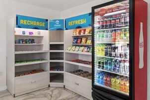 Una esquina de una tienda con estantes llenos de aperitivos, bebidas y un refrigerador.