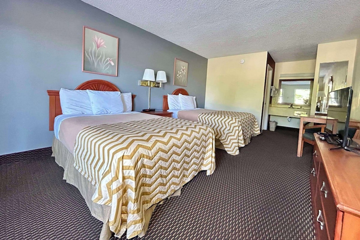 A hotel room with two beds, a desk, a chair, a television, and a bathroom visible through an open door.
