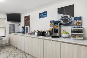 Un espace d’accueil d’hôtel équipé d’une machine à café, d’un appareil à gaufres et d’un panier de fruits.