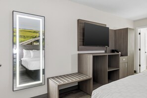 Une chambre d’hôtel avec un lit, un téléviseur fixé à un meuble en bois, un miroir reflétant un paysage et un petit banc en bois.