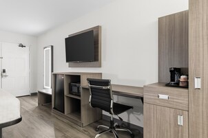 Habitación de hotel con cama, escritorio con televisor de pantalla plana, silla, cafetera y minibar.