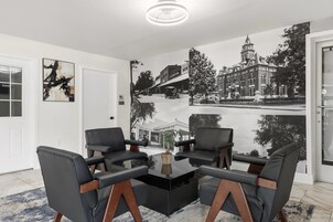 Una habitación con sofá de cuero negro, una mesa de centro de vidrio y un mural grande en blanco y negro que muestra una escena callejera.