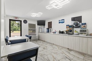 Una cafetería limpia y moderna con suelo de mármol, una barra con máquinas de café y un reloj en la pared.