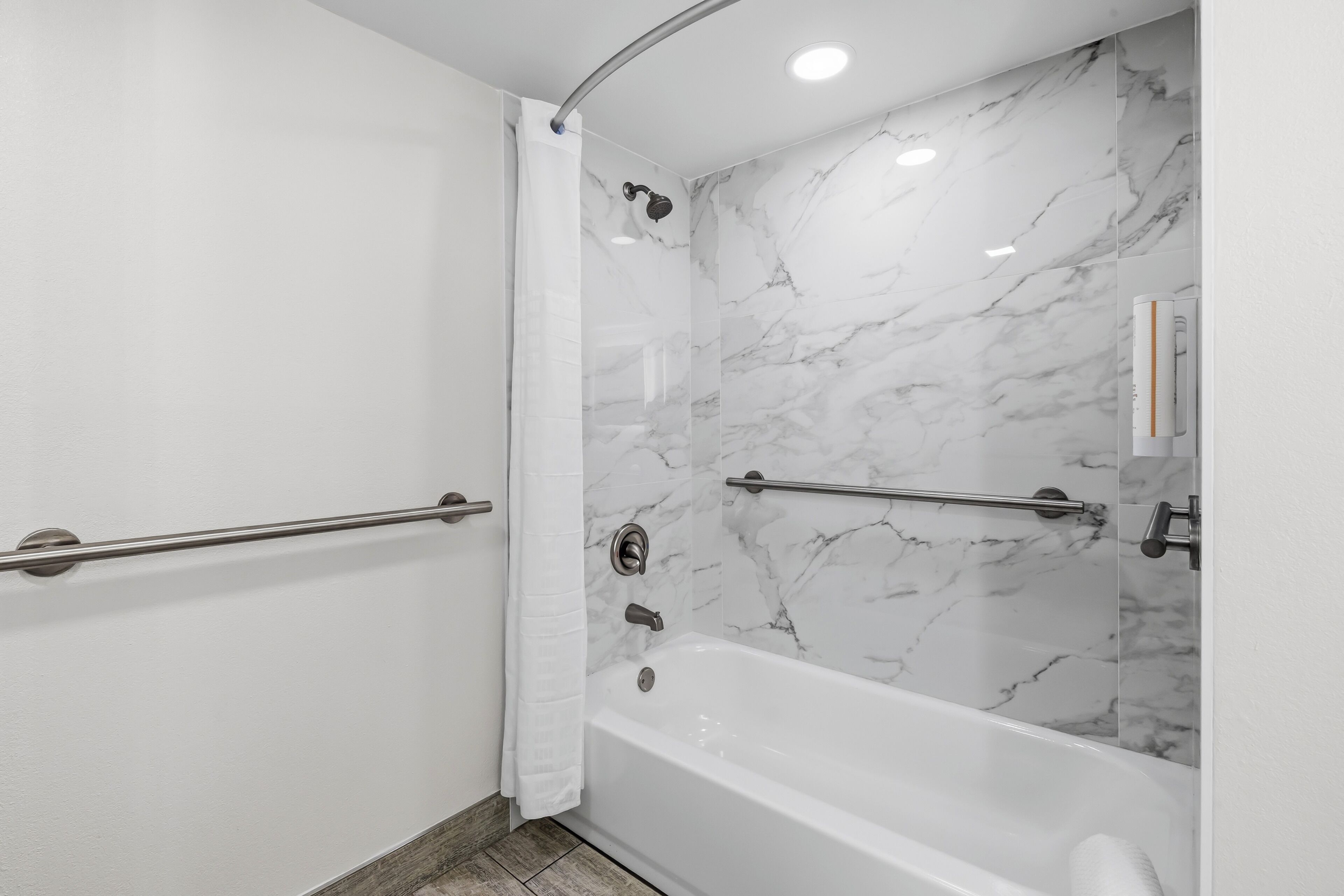 A modern bathroom with a marble shower wall, a bathtub, and a handrail.