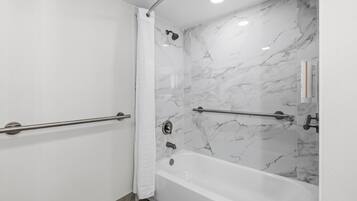A modern bathroom with a marble shower wall, a bathtub, and a handrail.