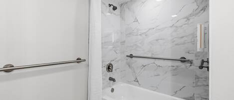 Un baño moderno con pared de ducha de mármol, bañera y barandilla.