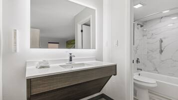 Une salle de bain moderne avec un grand miroir, un lavabo, une douche et des toilettes.