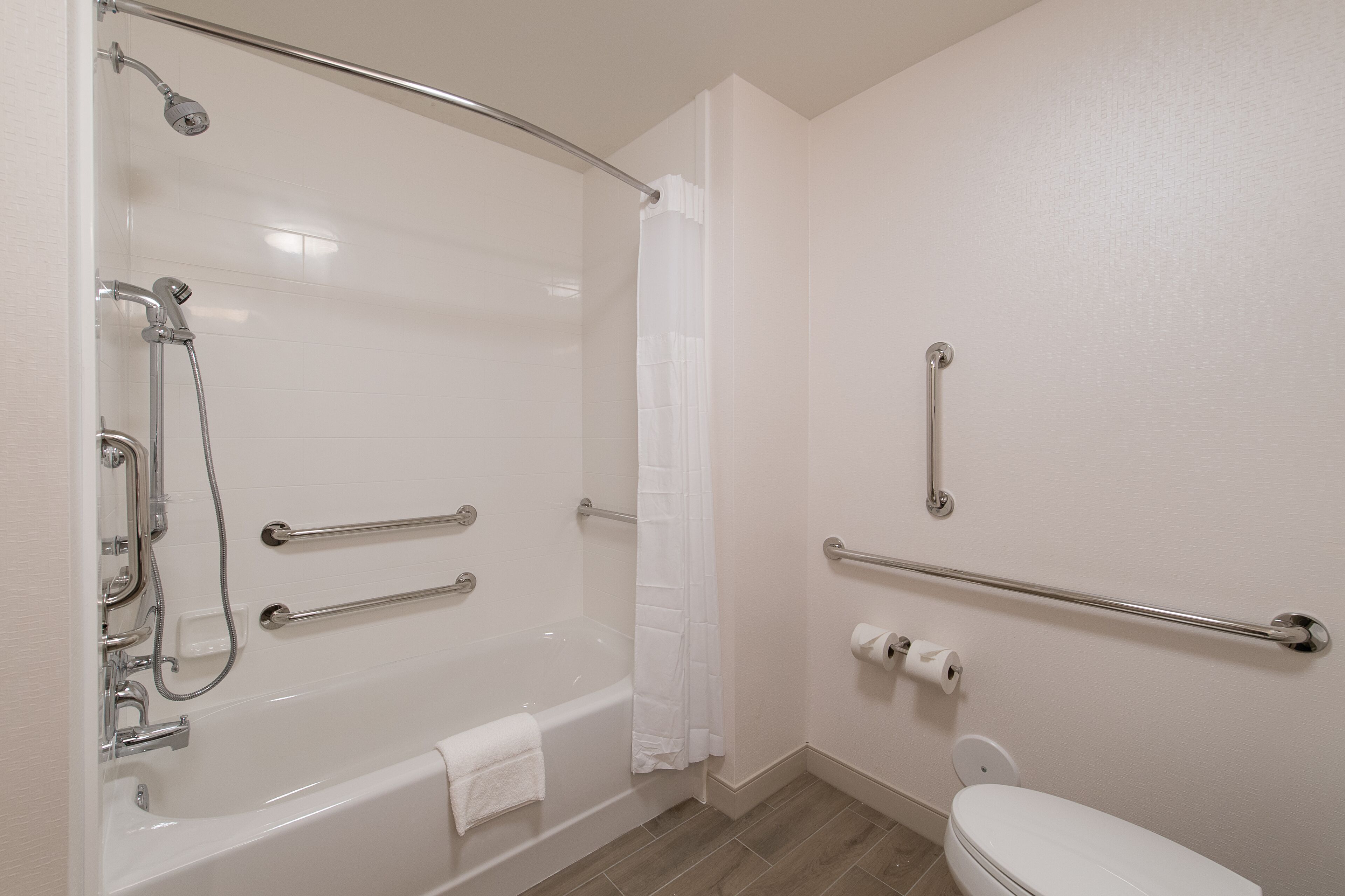 A bathroom with a bathtub, toilet, and handrails.