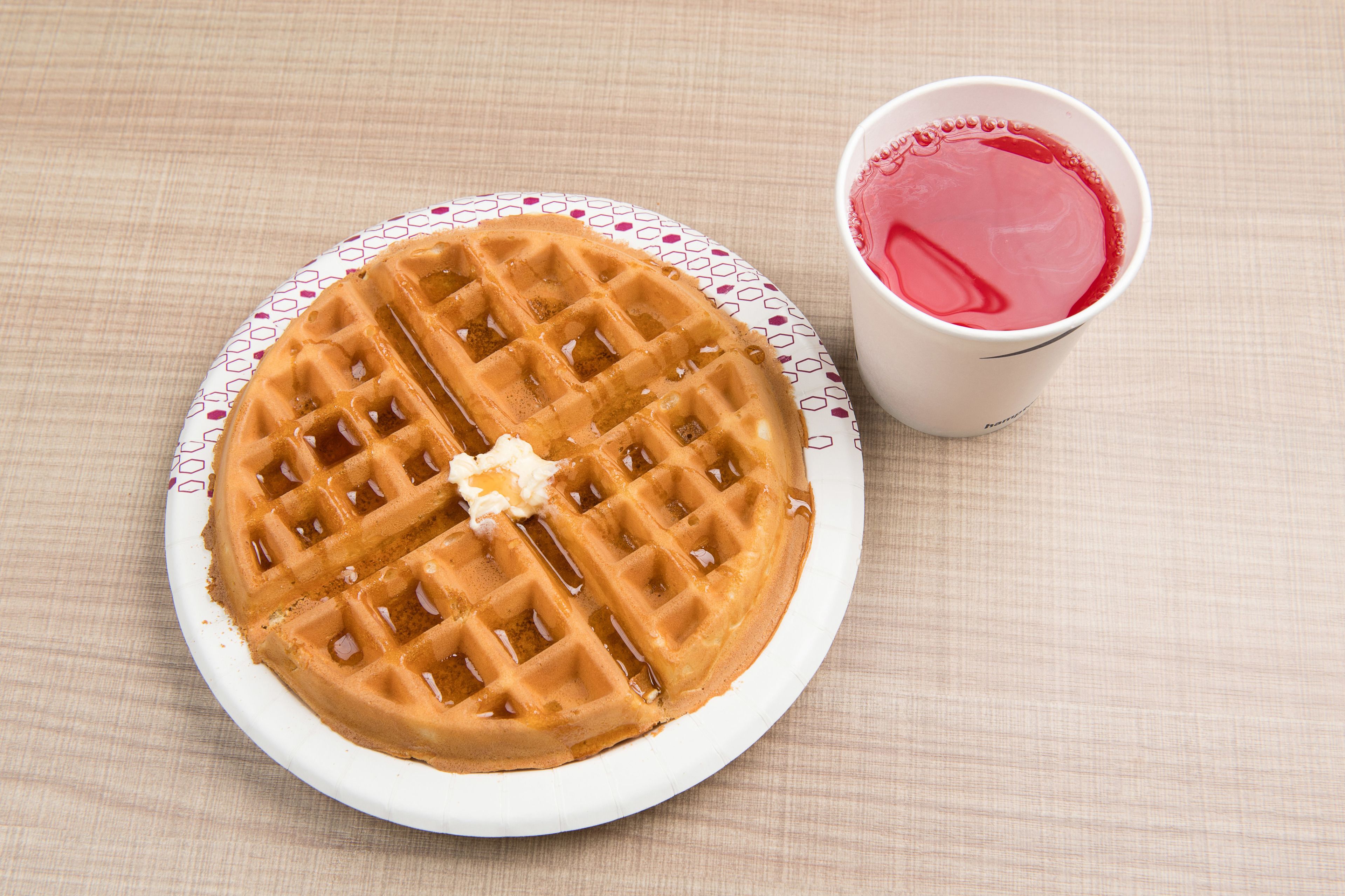 A plate with a waffle and a cup of red drink.