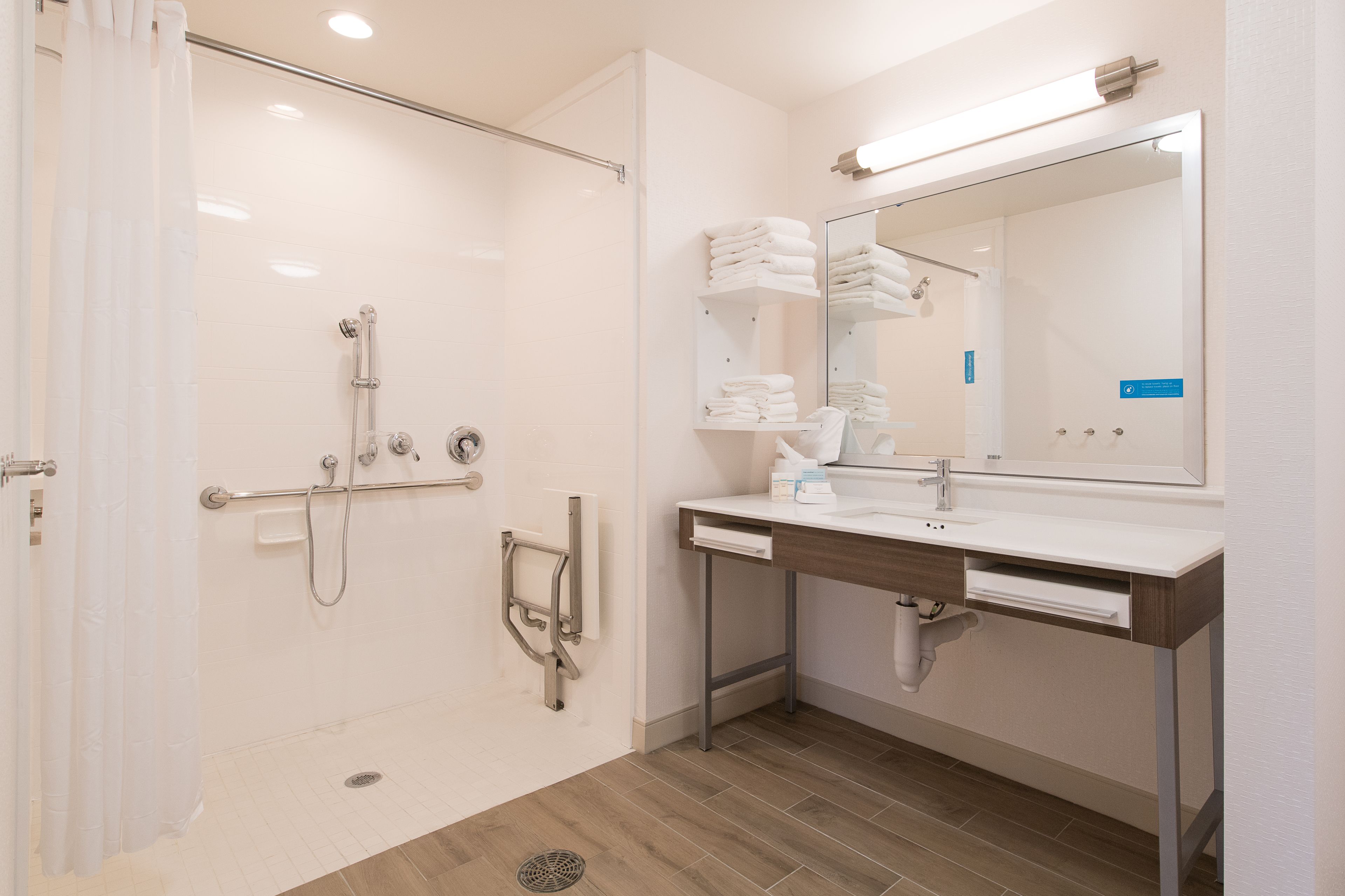 A modern bathroom with a walk-in shower, a vanity with a mirror, and neatly stacked towels.