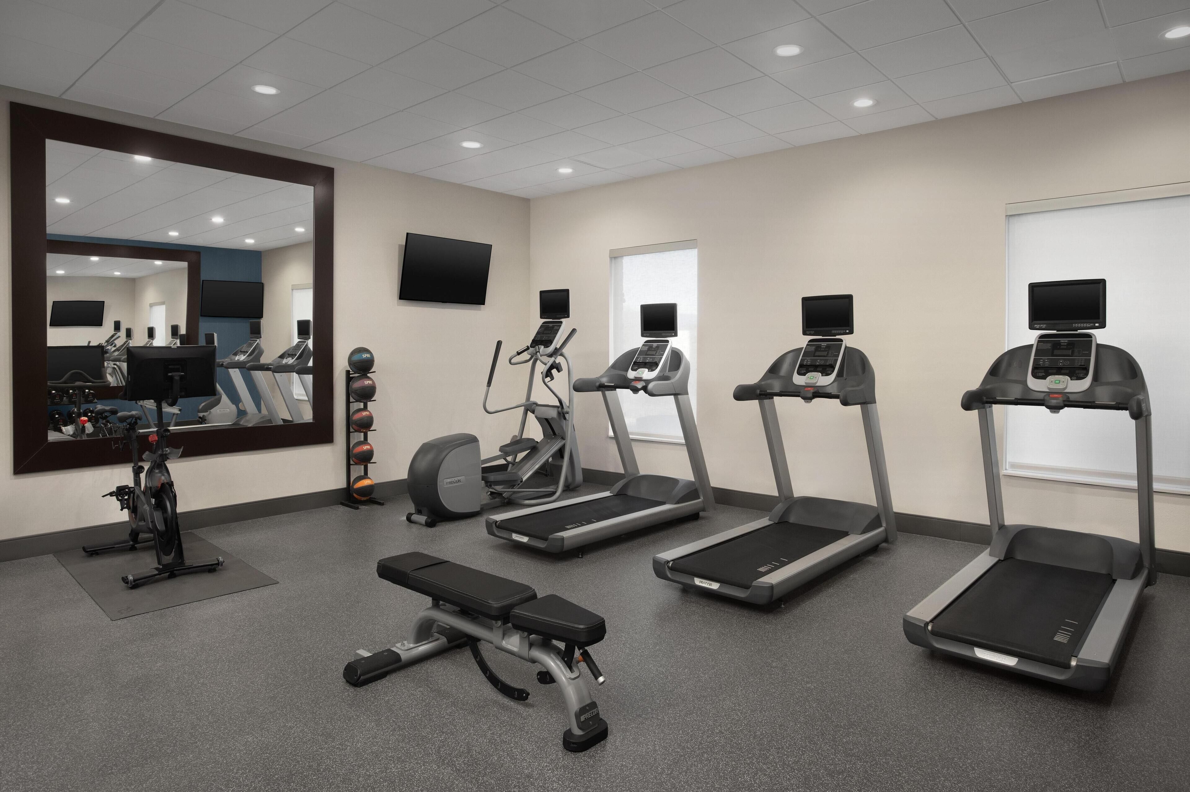 Un gimnasio con cintas de correr, elíptica, bicicleta estática y banco.