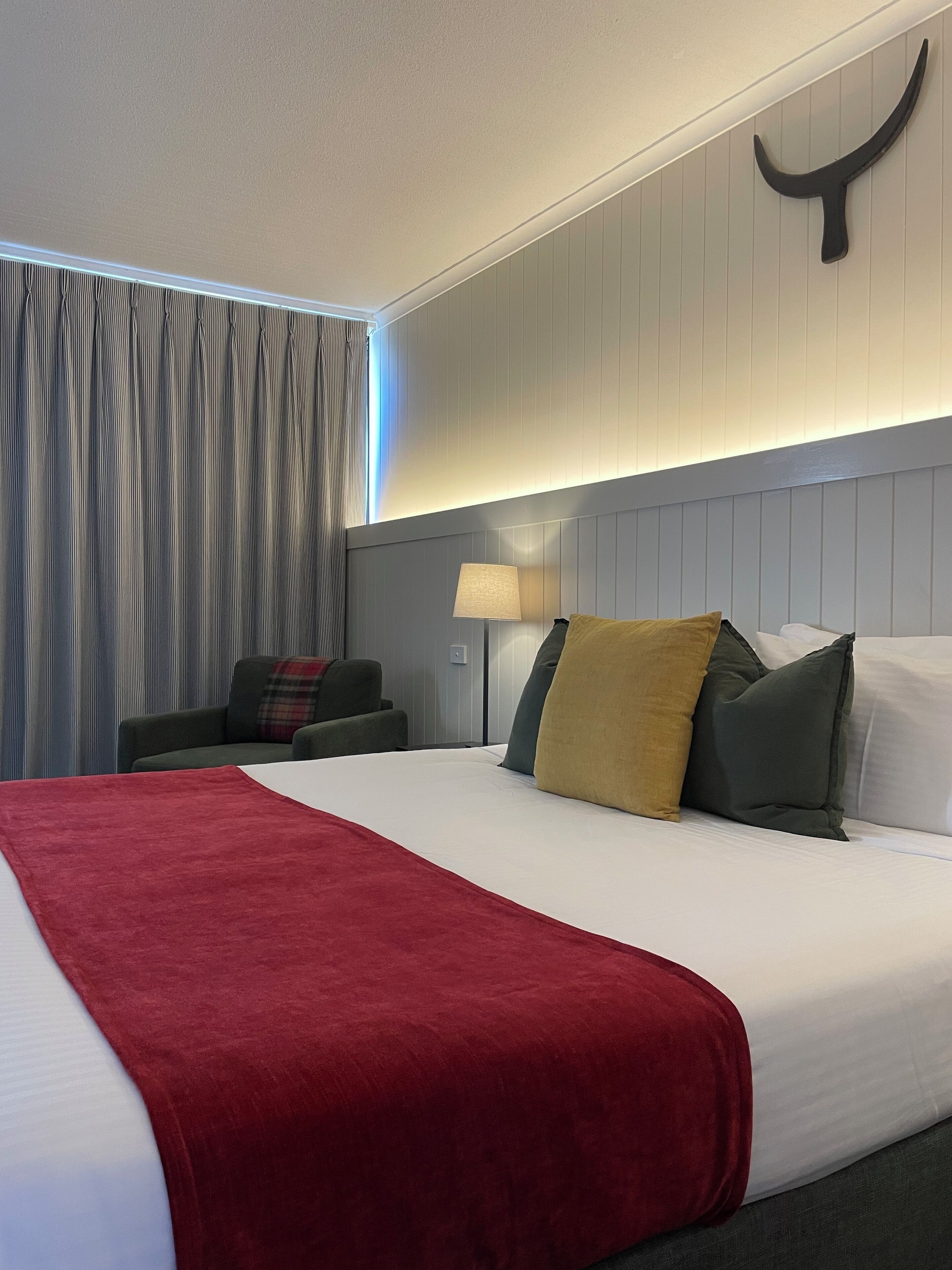 A hotel room with a large bed, a nightstand with a lamp, a chair, and a curtain.