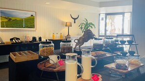 A breakfast buffet setup with various food items and beverages, a decorative horse sculpture, and a scenic painting on the wall.