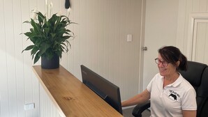 A reception desk with a laptop, a potted plant, and a pendant light.