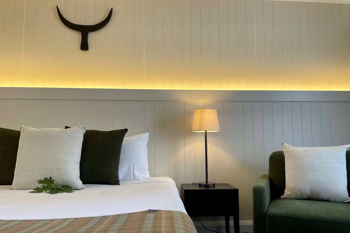 A hotel room with a bed, a nightstand, a lamp, and a green armchair.