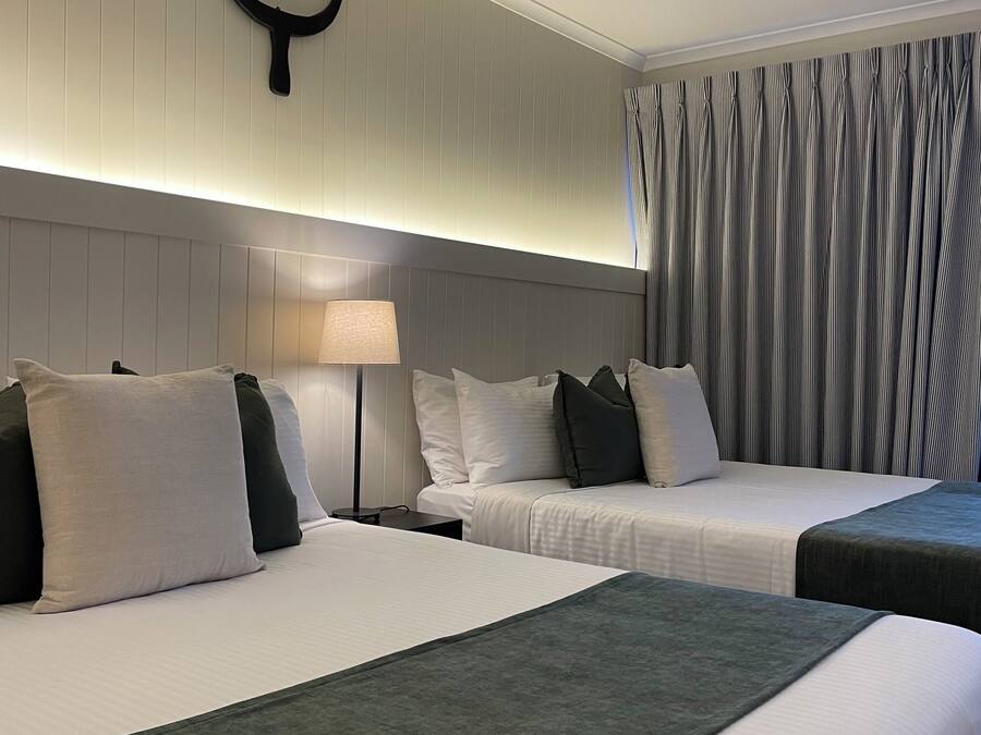 Habitación de hotel con dos camas, una mesita de noche, una lámpara y un aplique de pared.