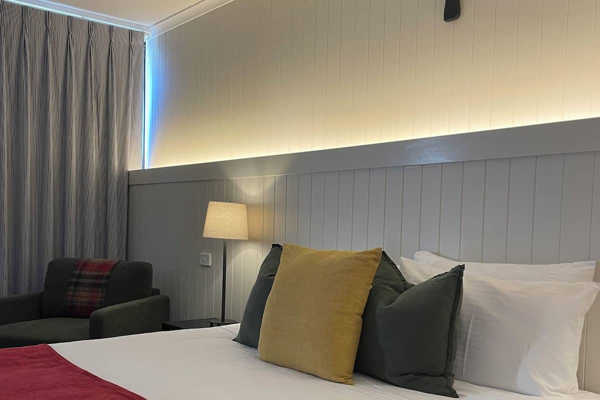 A hotel room with a large bed, a nightstand, a lamp, a couch, and a curtain.