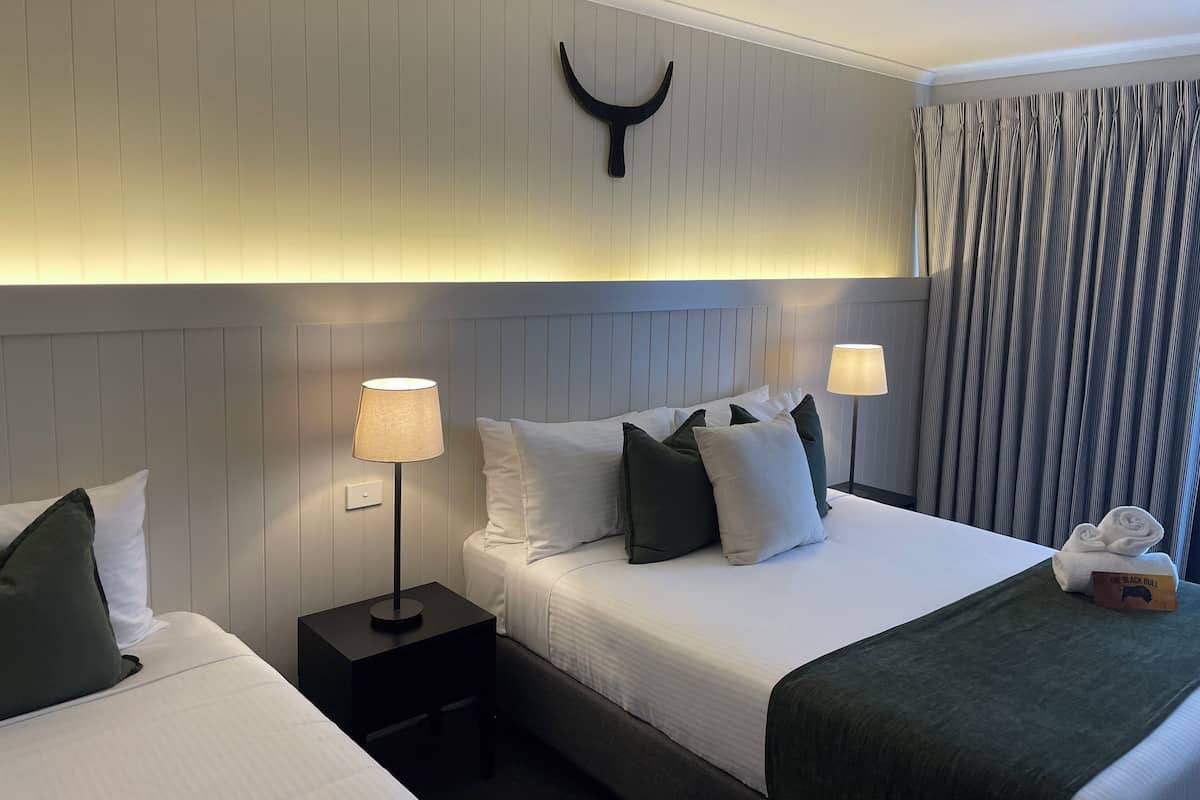 A hotel room with two beds, a headboard with a unique design, a nightstand with a lamp, and a curtain.