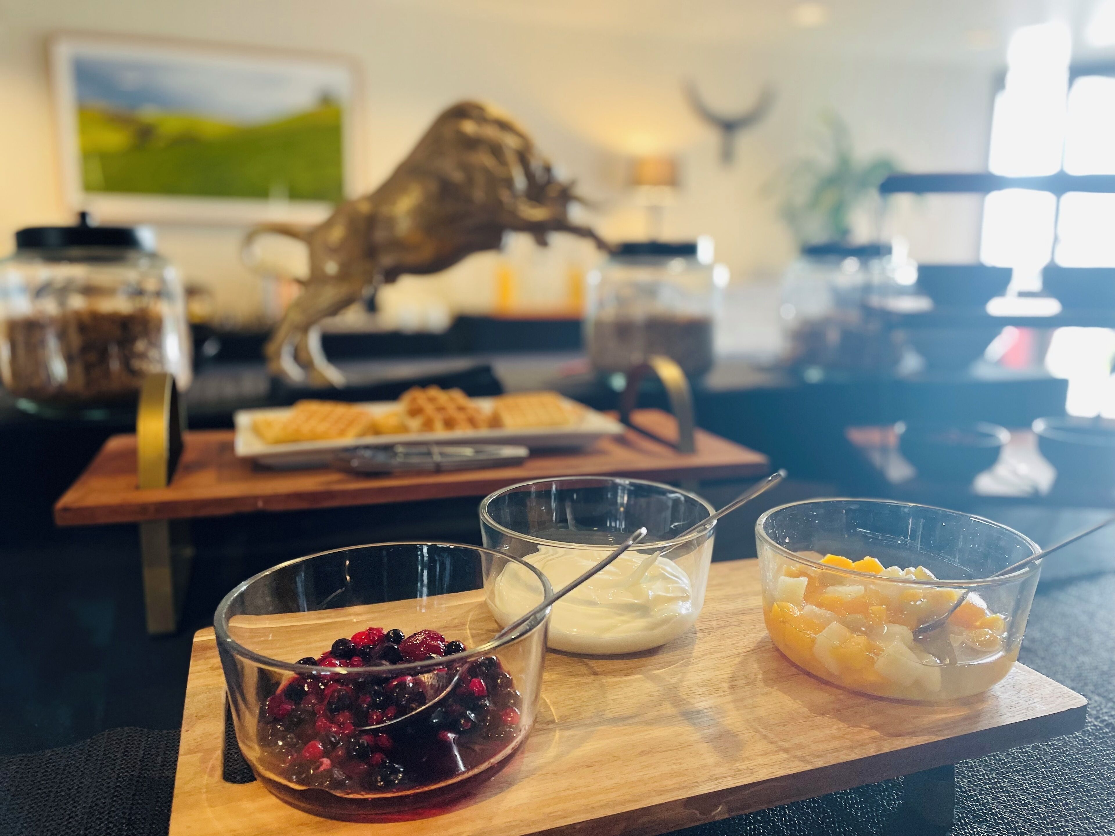 Una mesa de madera con tres tazones con distintos alimentos, un plato de gofres y una cabeza de venado decorativa.
