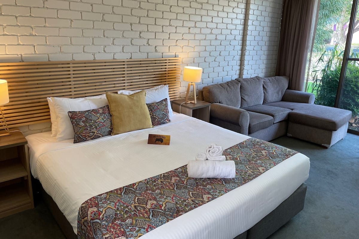 A hotel room with a bed, a sofa, a nightstand, and a window with curtains.