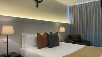 A hotel room with a bed, two bedside lamps, a headboard, a curtain, and a small table with a lamp.