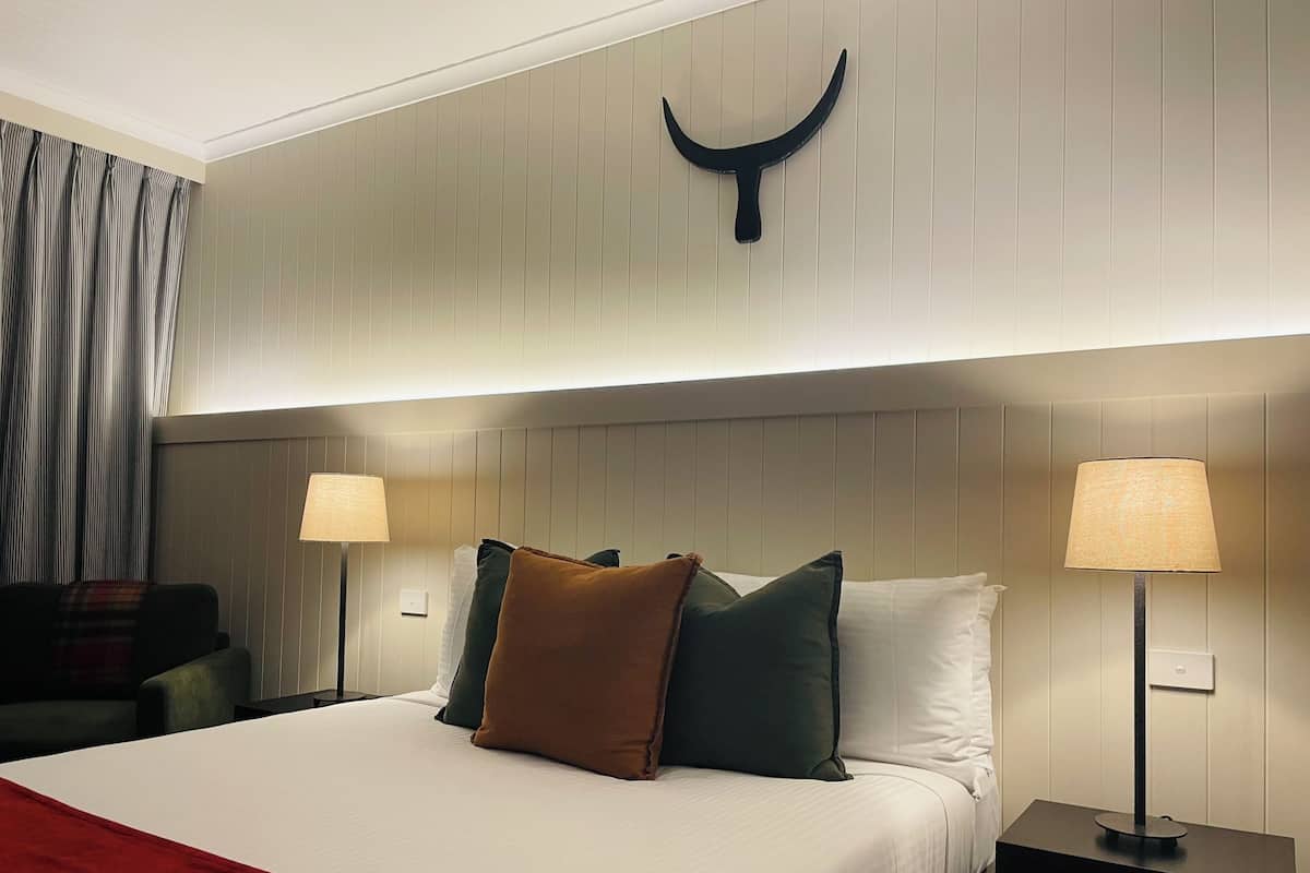 A hotel room with a bed, two bedside lamps, a headboard with a horn-shaped decoration, and a red throw blanket.