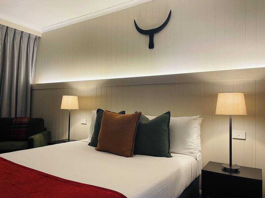 Een hotelkamer met een bed, twee bedlampen, een hoofdbord met een decoratieve hoorn en een rode plaid.