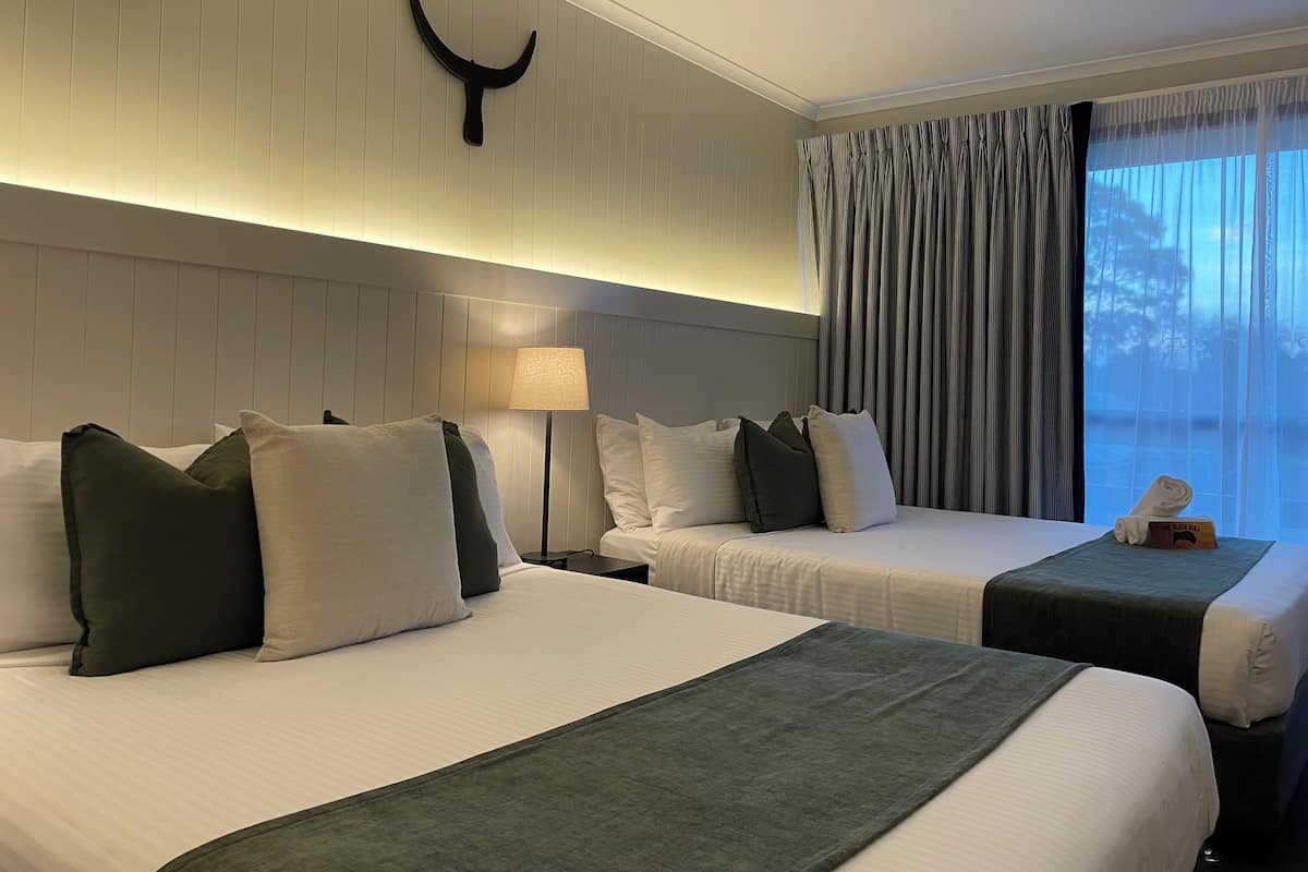 A hotel room with two beds, a nightstand, a lamp, a wall-mounted decoration, and a window with curtains.