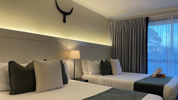 A hotel room with two beds, a nightstand, a lamp, a wall-mounted decoration, and a window with curtains.