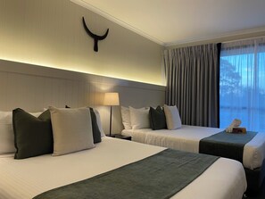 A hotel room with two beds, a nightstand, a lamp, a wall-mounted decoration, and a window with curtains. - The Black Bull Motel (Traralgon)