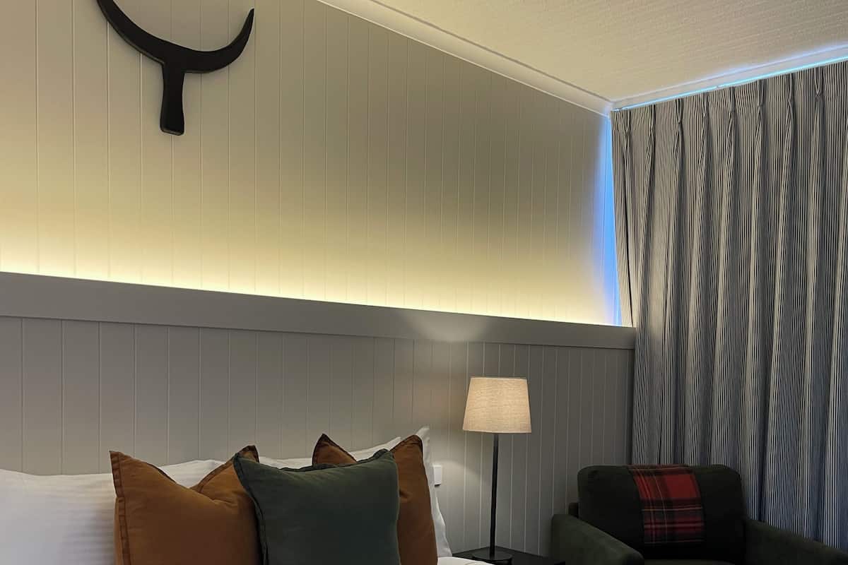 A hotel room with a large bed, a nightstand with a lamp, a chair, and a wall-mounted light fixture.