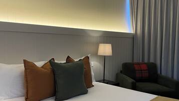 Ein Hotelzimmer mit einem großen Bett, einem Nachttisch mit Lampe, einem Sessel und einer Wandleuchte.