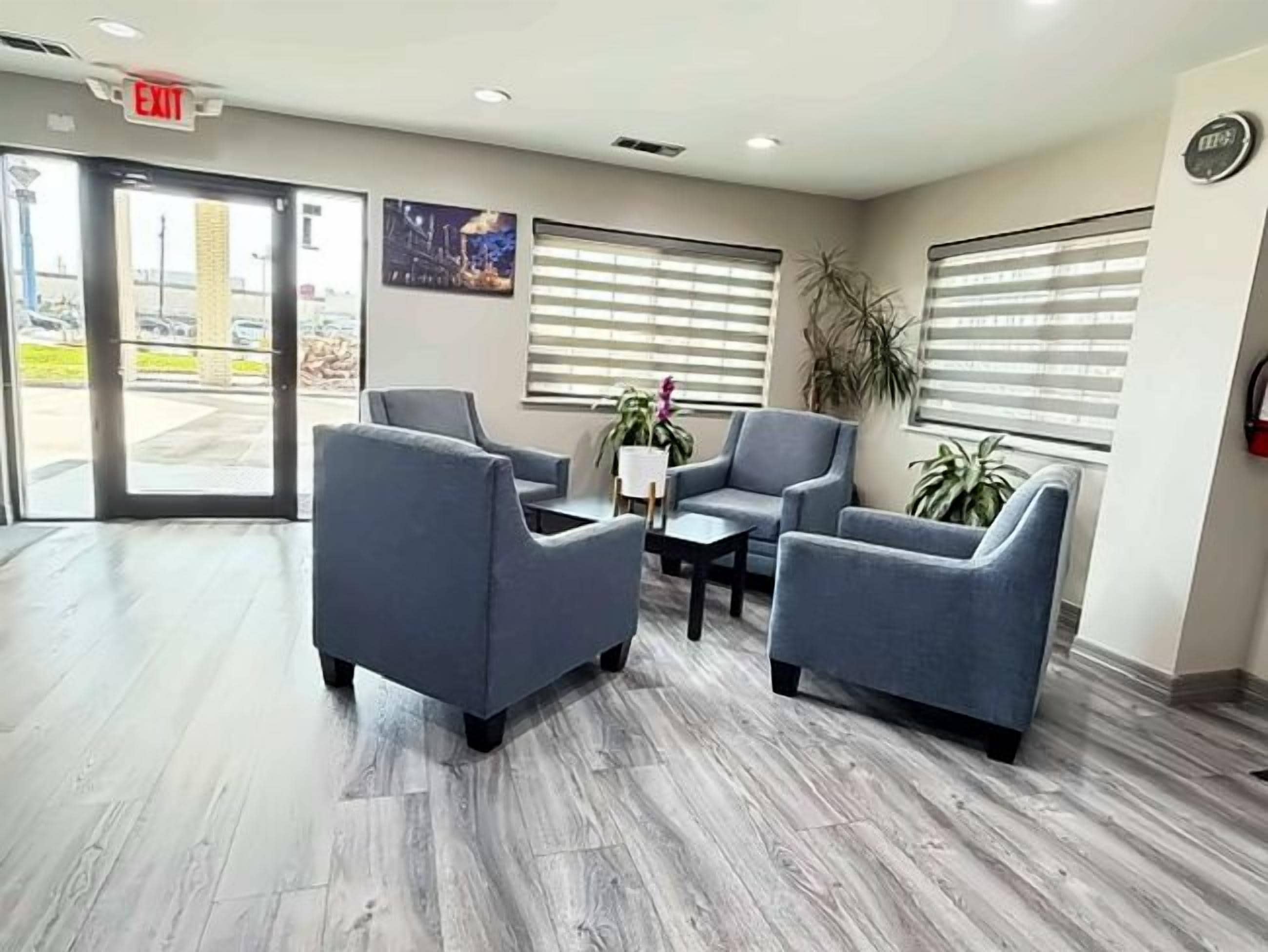 A reception area with a wooden floor, two blue armchairs, a small table, and a potted plant.