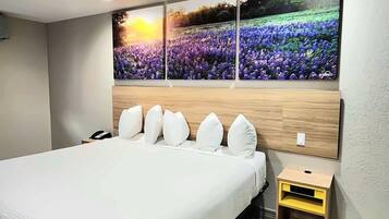 A hotel room with a large bed, a bedside table, and a wall-mounted artwork of a field of flowers.