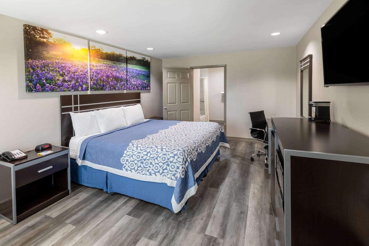 A hotel room with a bed, a desk, a chair, a TV, and a painting of flowers.